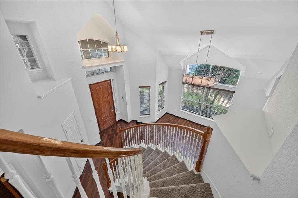 512 Renfro Court, Irving, TX 75063 Curved staircase featuring a wooden handrail and white balusters, vaulted ceilings, arched windows, wood-finish flooring, and multi-light hanging fixtures