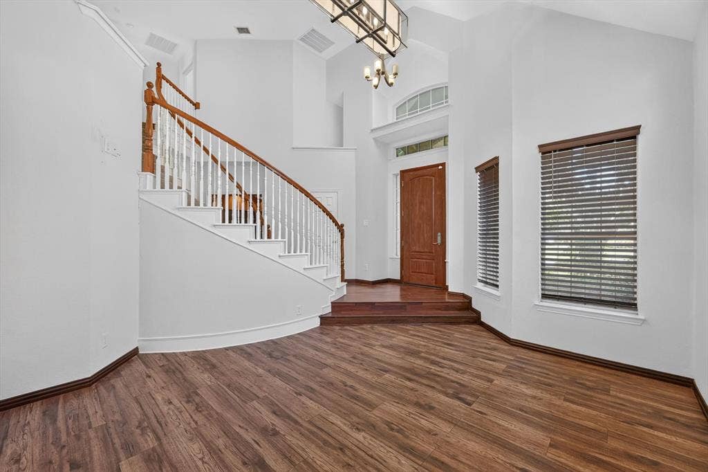 512 Renfro Court, Irving, TX 75063 Foyer featuring vaulted ceilings, wood-finish flooring, a curved staircase with wooden handrail, arched transom window, and chandelier
