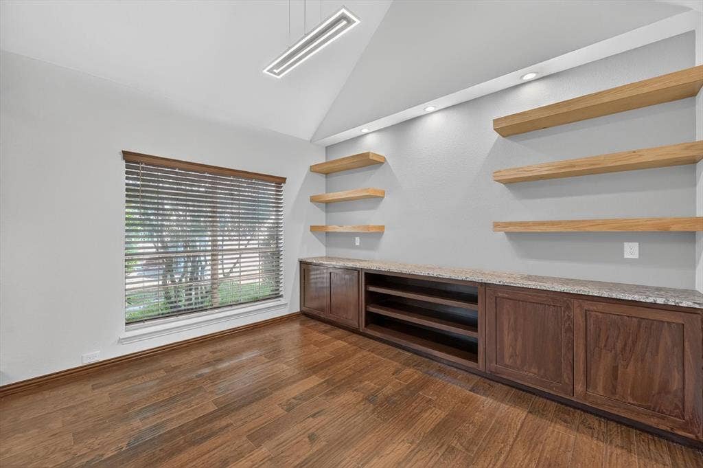 512 Renfro Court, Irving, TX 75063 Vaulted ceiling, built-in cabinetry with stone-finish countertops, natural wood floating shelves, recessed lighting, and wood-finish flooring