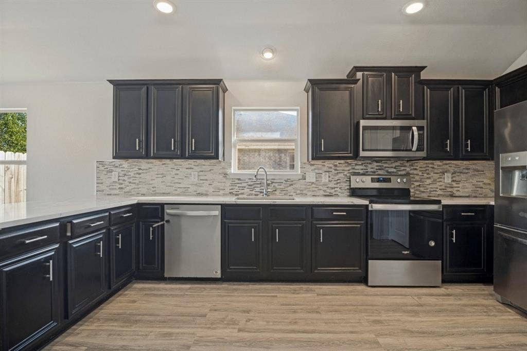 2815 Briarbrook Drive, Seagoville, TX 75159 Kitchen featuring dark wood cabinetry, light countertops, wood-finish flooring, a mosaic tile backsplash, and stainless steel appliances