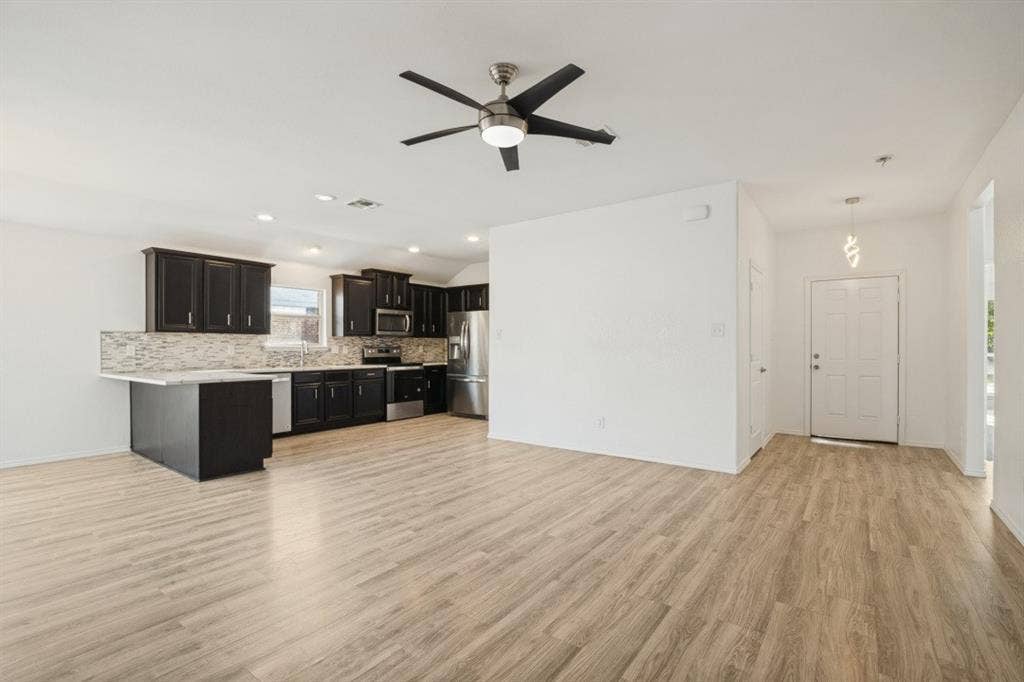 2815 Briarbrook Drive, Seagoville, TX 75159 Open-concept common area featuring wood-finish flooring, dark wood cabinetry, a mosaic tile backsplash, and stainless steel appliances