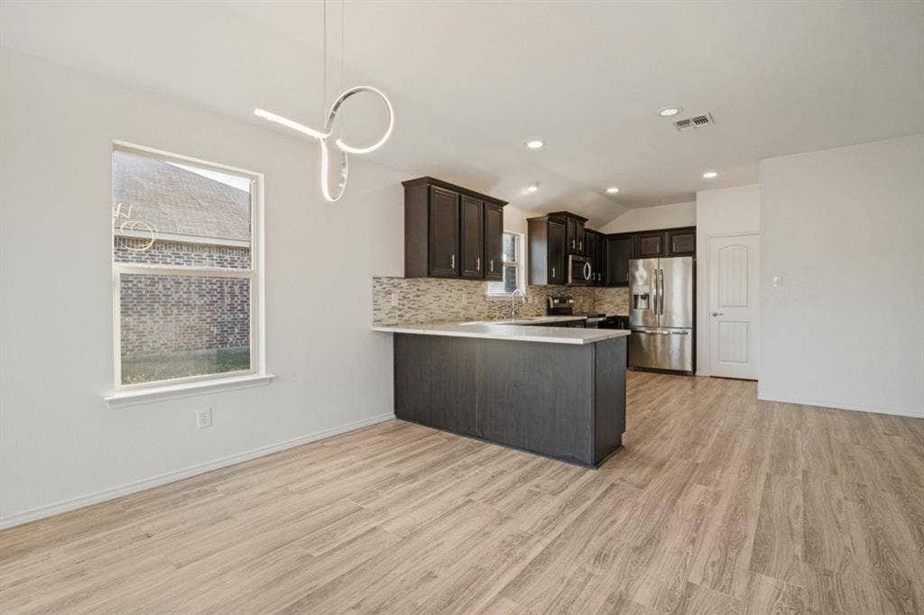 2815 Briarbrook Drive, Seagoville, TX 75159 Open-concept living space featuring wood-finish flooring, a contemporary pendant light fixture, dark wood cabinetry, a mosaic tile backsplash, and stainless steel appliances