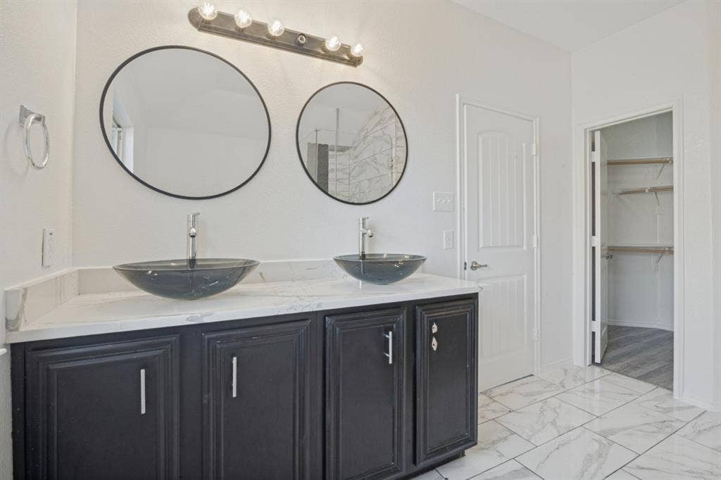 2815 Briarbrook Drive, Seagoville, TX 75159 Dual vessel sinks, black cabinetry, white countertop, two circular mirrors, and tile flooring