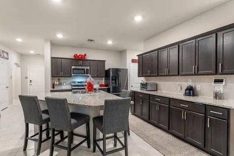 Kitchen featuring dark wood-finish cabinetry, granite-style countertops, stainless steel appliances, and recessed lighting