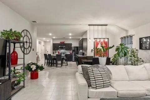Expansive open-concept living area featuring light-toned tile flooring, recessed lighting, and a modern kitchen with dark cabinetry