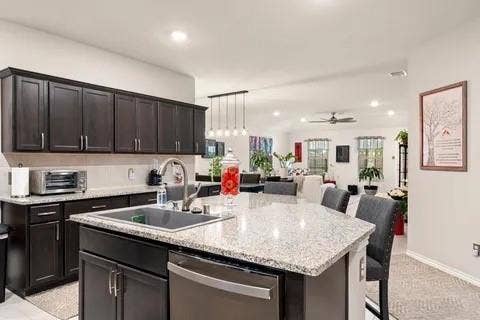 Kitchen featuring dark wood cabinetry, light granite countertops, a stainless steel sink, and a stainless steel dishwasher
