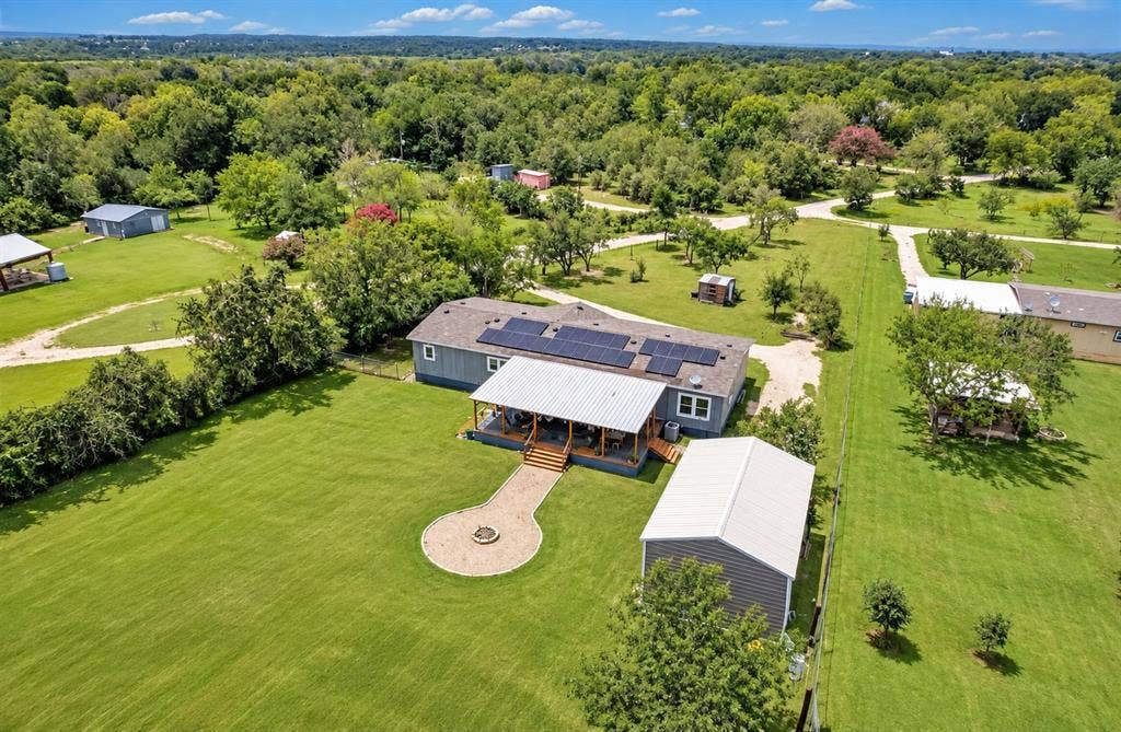 213 River Front Drive, Cedar Creek, TX 78612 Expansive green lawn with a gravel pathway leading to a fire pit, covered porch with wood decking, and a separate structure with a metal roof