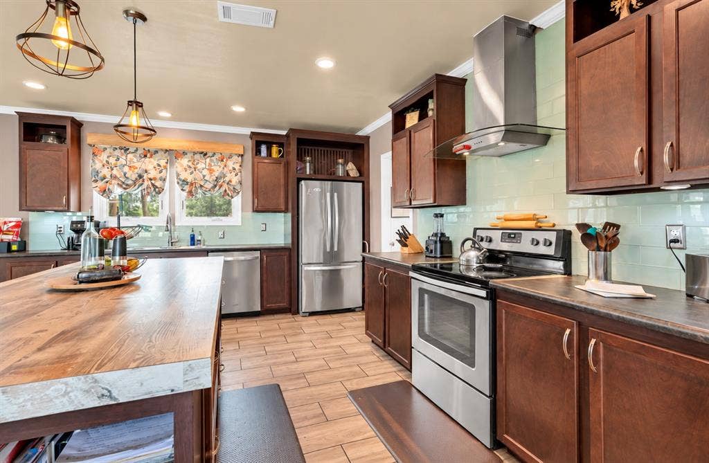 213 River Front Drive, Cedar Creek, TX 78612 Wood-finish island with a contrasting stone-finish countertop, wood-finish cabinetry, stainless steel appliances, light-toned tile backsplash, and recessed lighting