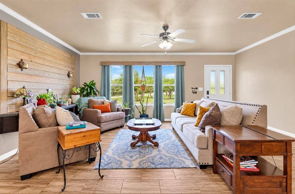 213 River Front Drive, Cedar Creek, TX 78612 Wood-finish flooring, accent wall with horizontal wood paneling, crown molding, ceiling fan, and multiple windows