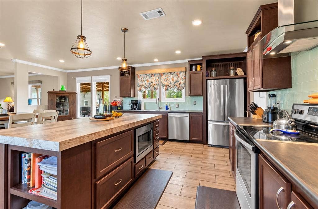 213 River Front Drive, Cedar Creek, TX 78612 Kitchen featuring a center island with built-in microwave, wood-finish cabinetry, stainless steel appliances, tile flooring, and a subway tile backsplash
