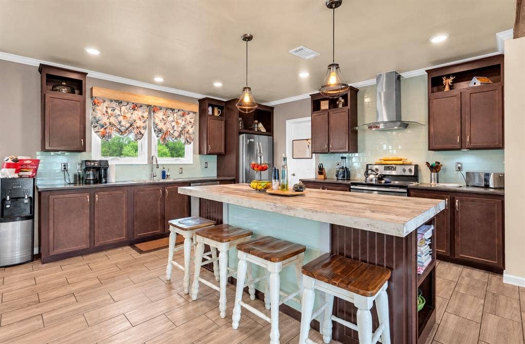 213 River Front Drive, Cedar Creek, TX 78612 Kitchen with wood-finish flooring, dark wood cabinetry, a light blue tile backsplash, a stainless steel range hood, and a built-in island with a light-toned countertop
