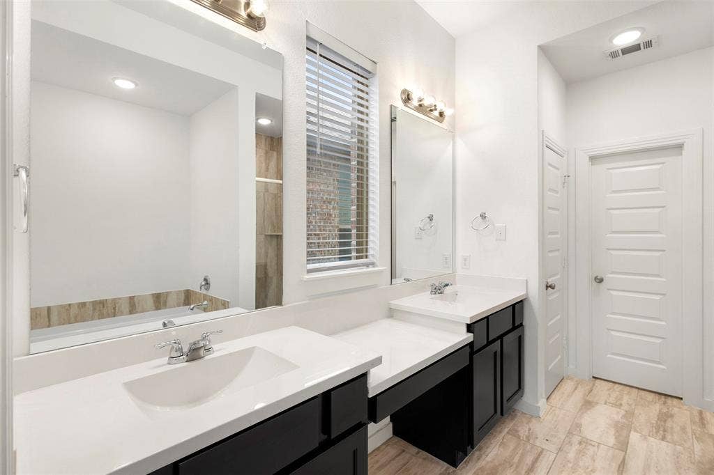 2466 San Marcos Drive, Forney, TX 75126 Dual vanity with dark cabinetry, light-toned composite countertops, large wall-mounted mirrors, and tile flooring