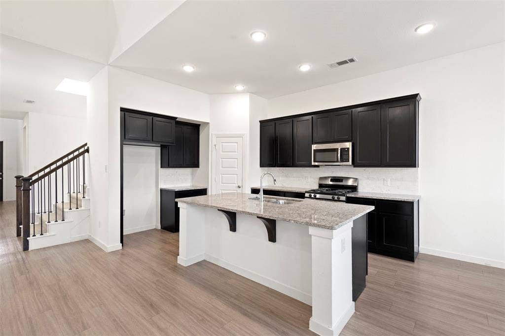 2466 San Marcos Drive, Forney, TX 75126 Kitchen featuring dark cabinetry, stone-finish countertops, a central island with a sink, recessed lighting, and wood-finish flooring