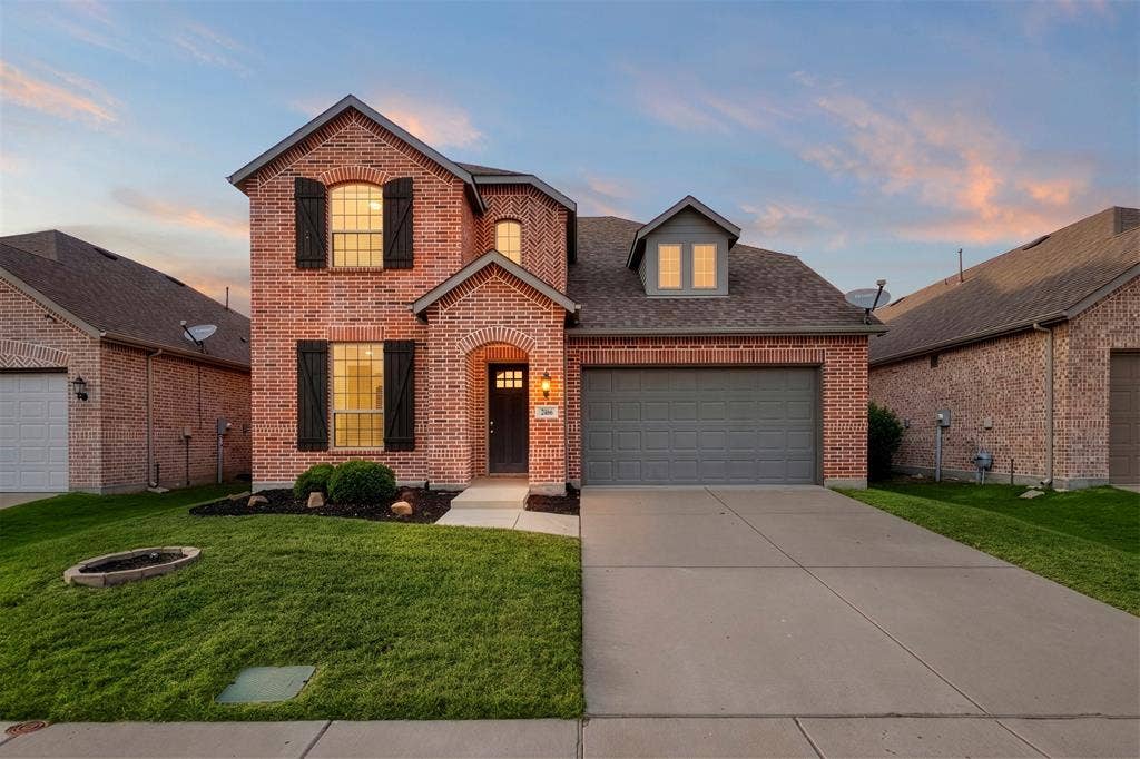 2466 San Marcos Drive, Forney, TX 75126 Two-story brick exterior featuring a shingled roof, decorative shutters, a covered arched entryway, and an attached two-car garage