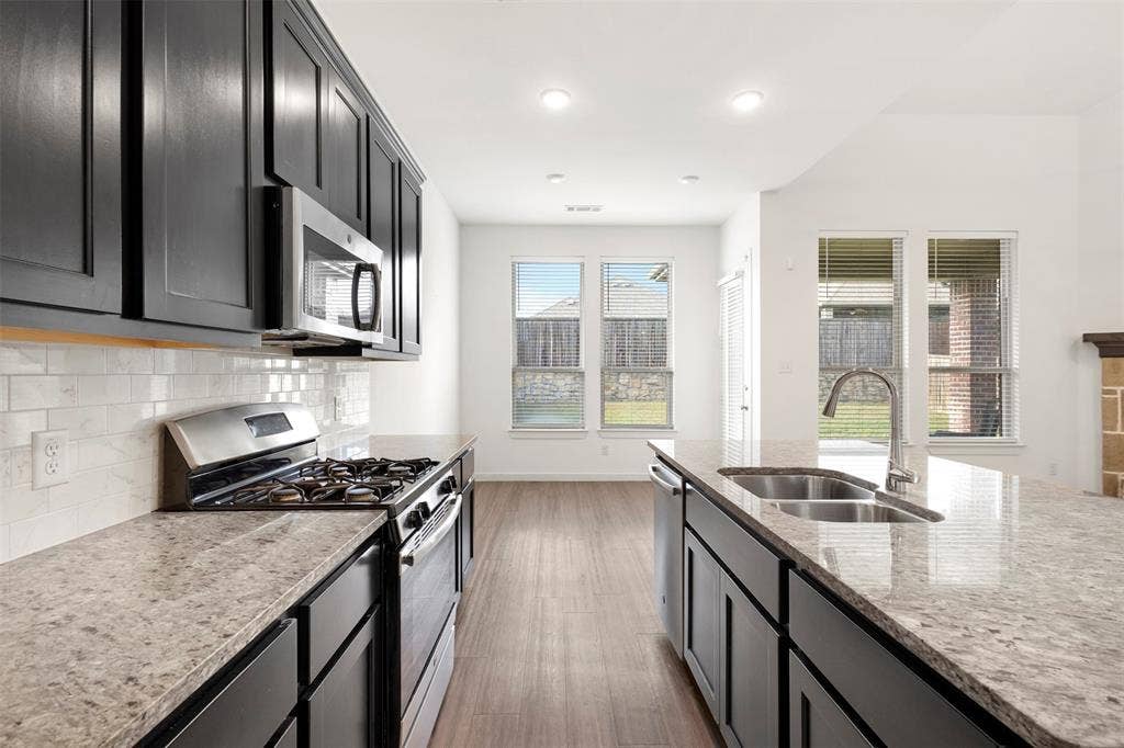 2466 San Marcos Drive, Forney, TX 75126 Kitchen featuring dark cabinetry, stone-finish countertops, stainless steel appliances, subway tile backsplash, and wood-finish flooring
