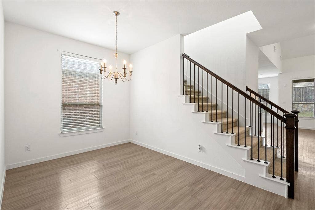 2466 San Marcos Drive, Forney, TX 75126 Open-concept space featuring wood-finish flooring, a traditional multi-arm chandelier, and a staircase with a dark wood handrail and black iron balusters