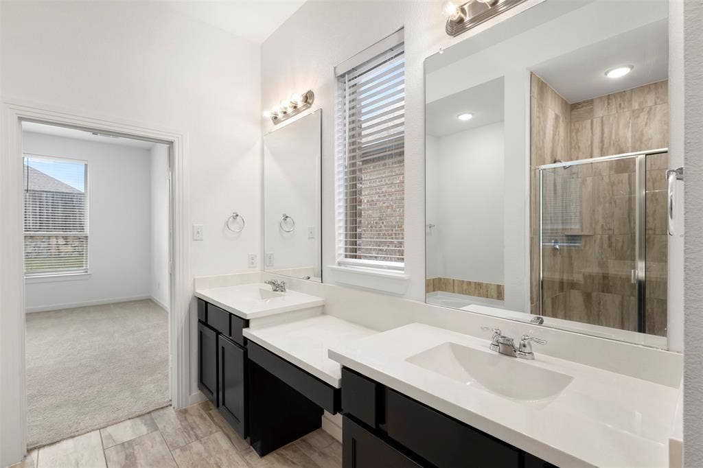 2466 San Marcos Drive, Forney, TX 75126 Dual-sink vanity with dark cabinetry and stone countertops, glass-enclosed shower featuring tiled surround, and large wall-mounted mirrors