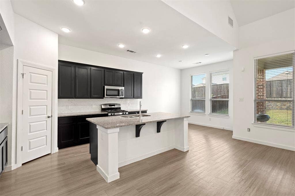 2466 San Marcos Drive, Forney, TX 75126 Kitchen featuring black cabinetry, stone-surface countertops, central island, wood-finish flooring, and vaulted ceilings