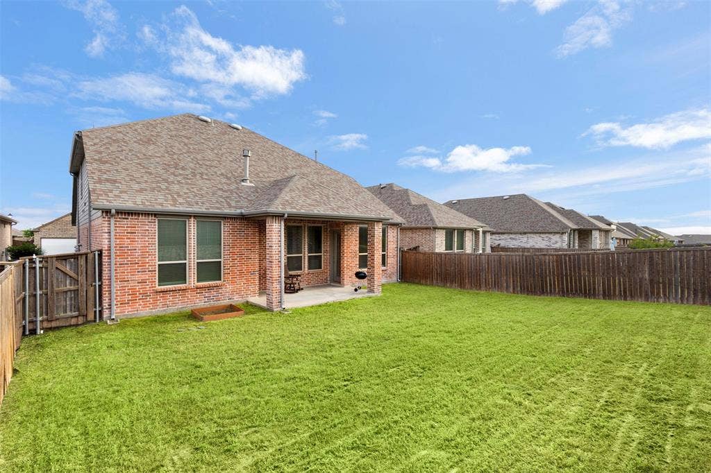 2466 San Marcos Drive, Forney, TX 75126 Rear exterior featuring red brick masonry, a covered concrete patio, a private fenced yard, and a shingled roof