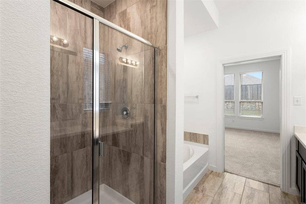 2466 San Marcos Drive, Forney, TX 75126 Walk-in shower with wood-patterned tile surround, glass enclosure, chrome shower fixture, soaking tub, and tile flooring