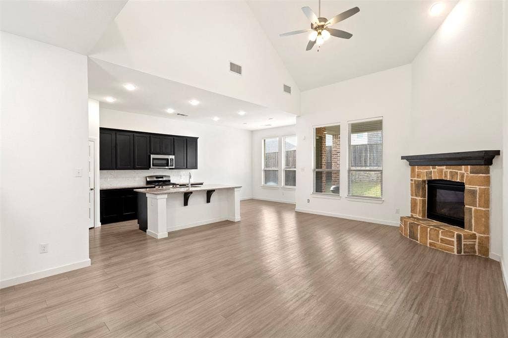 2466 San Marcos Drive, Forney, TX 75126 Vaulted ceilings featuring recessed lighting, a stone-surround fireplace with a wooden mantel, wood-finish flooring, and a kitchen equipped with dark cabinetry and a central island