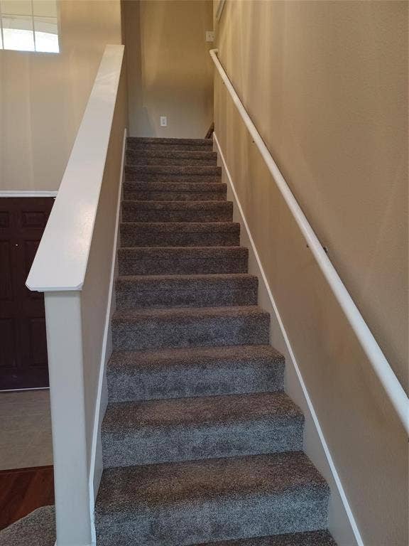 Carpeted staircase with a white handrail and a window providing natural light