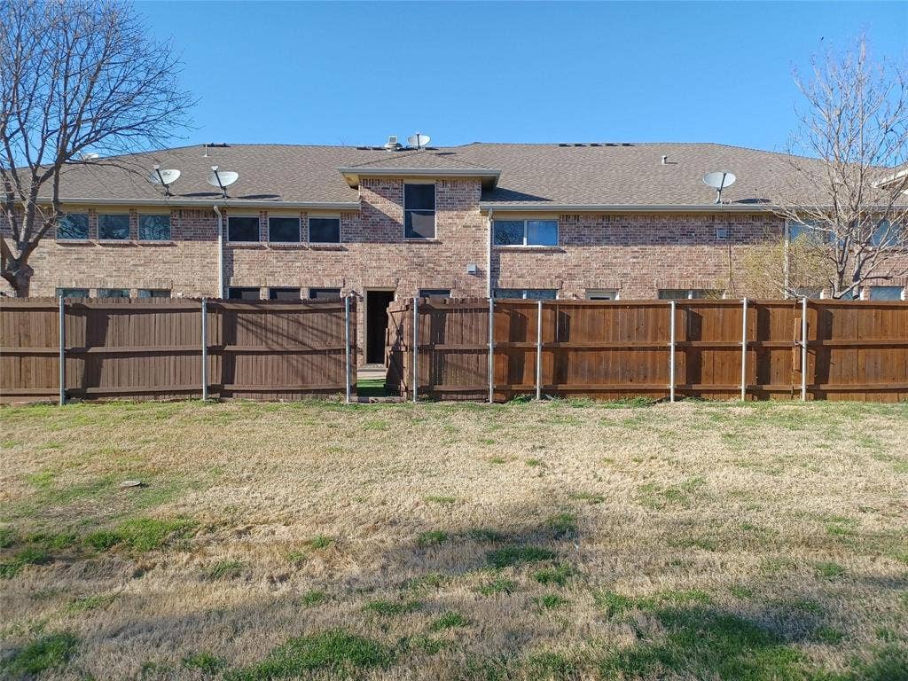 Brick exterior, brown fencing, multiple windows, and a shingle roof