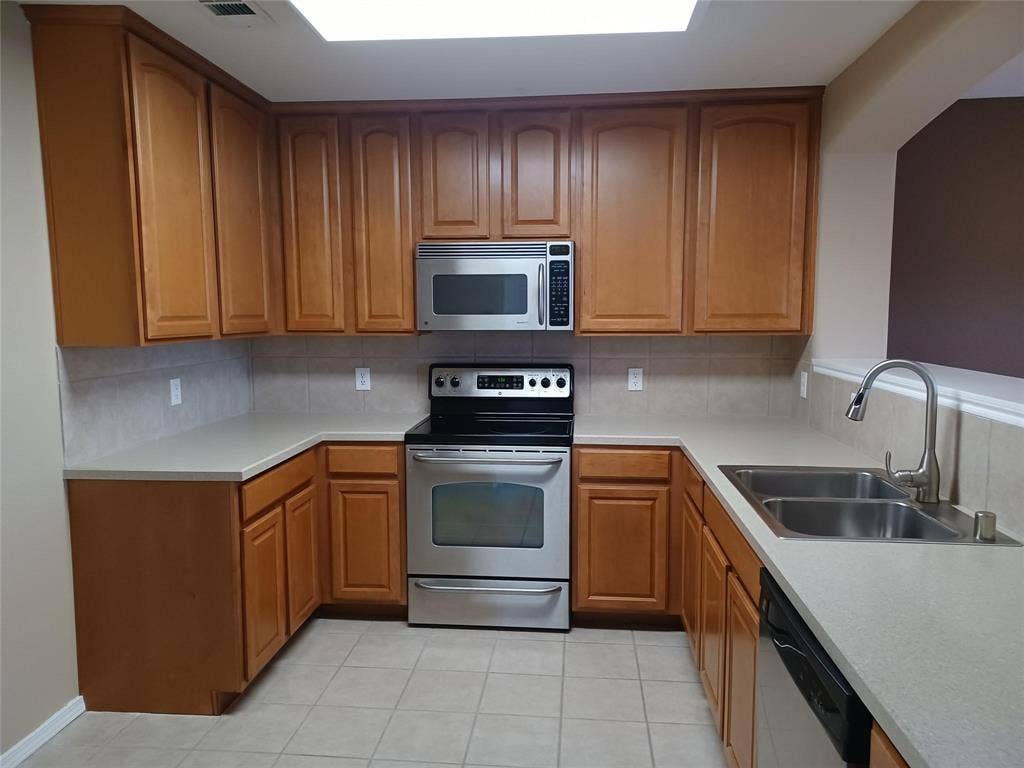 U-shaped kitchen featuring wood cabinetry, stainless steel appliances, light-toned countertops, tile backsplash, and tile flooring