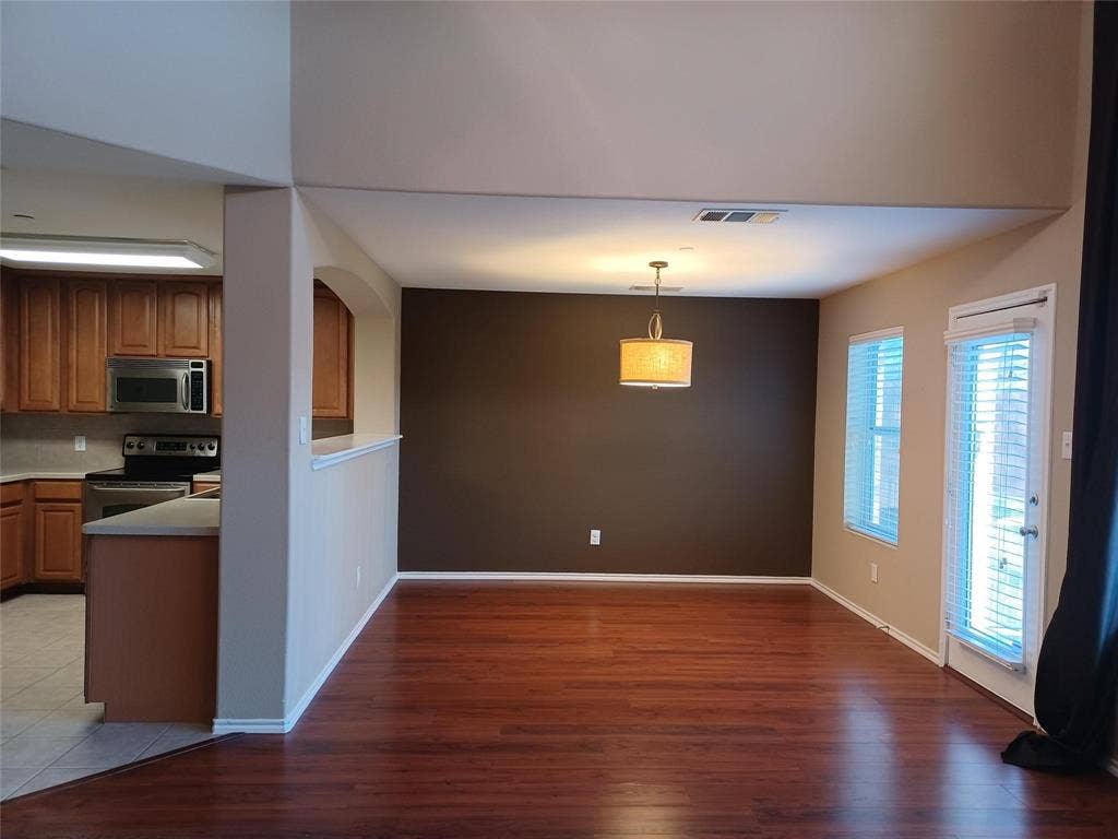 Open-concept living area with wood-finish flooring, a contemporary chandelier, two windows, and an exterior door with integrated blinds