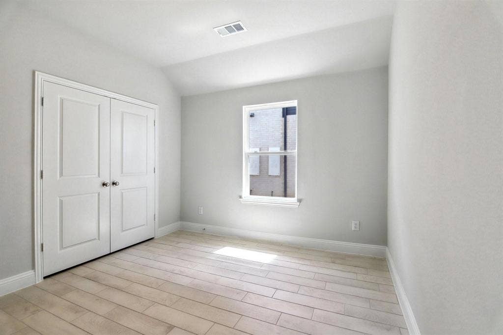 Light-toned wood-finish flooring, crisp white walls, single window, and double panel doors