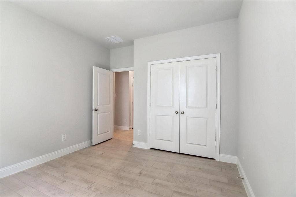 Light wood-finish flooring with white baseboards, a bi-fold closet with panel doors, and a paneled entry door