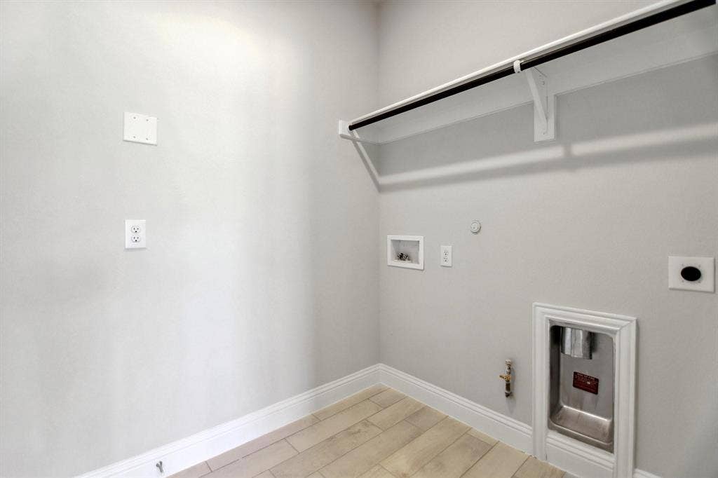 Wood-finish flooring with white baseboards, a built-in shelf and rod, and hookups for appliances