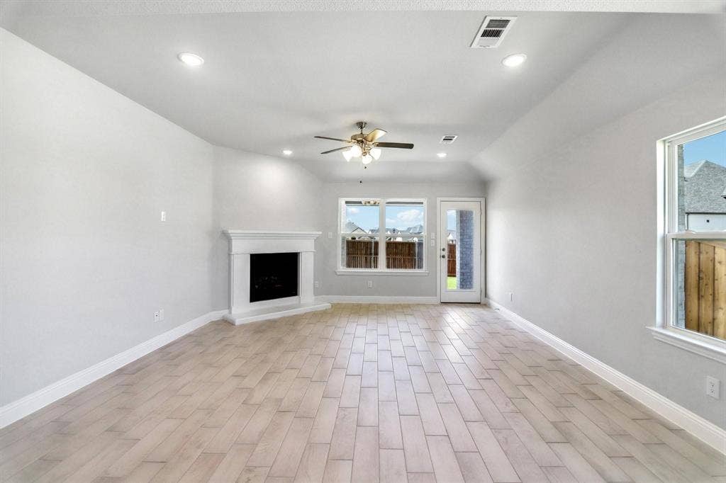Spacious room featuring wood-finish flooring, a built-in fireplace with a white mantel, recessed lighting, a ceiling fan, and multiple windows
