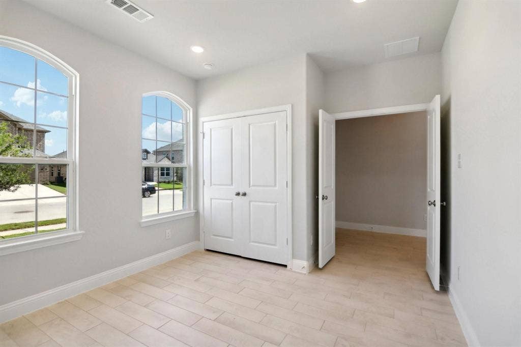 Light-toned wood-finish flooring, two arched windows with gridded panes, built-in double-door closet, and recessed ceiling lighting