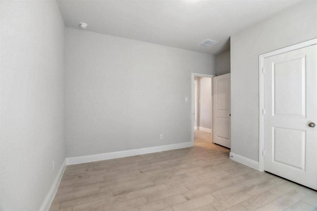 Light-toned wood-finish flooring, white trim, and a white interior door with a silver-toned knob