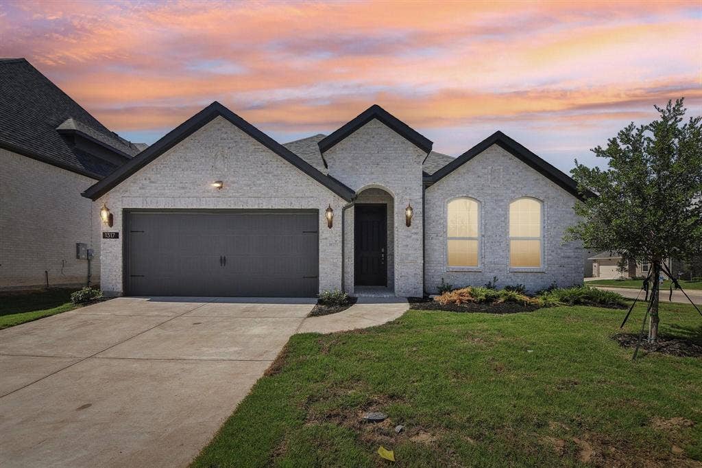 Exterior featuring a light brick facade, dark trim, arched entry, two-car garage, and established landscaping