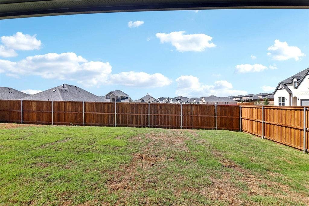 Expansive outdoor space featuring a wood fence, green lawn, and residential roofs in the background