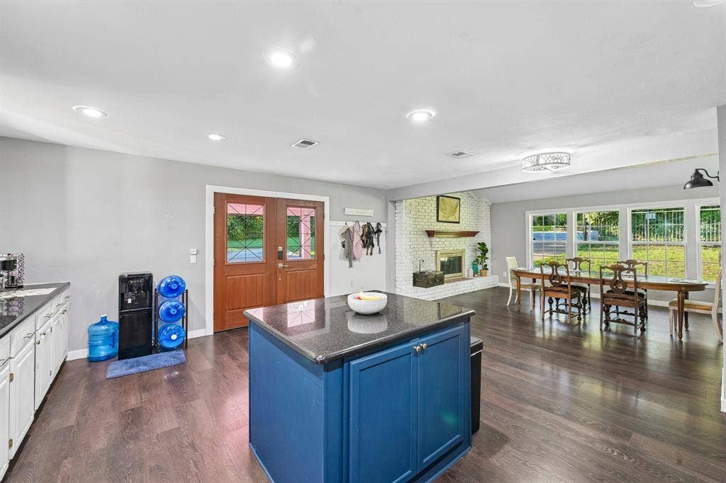 500 Spinner Road, DeSoto, TX 75115 Wood-finish flooring throughout, featuring a kitchen island with storage and a dark countertop, white perimeter cabinetry, and an exposed brick fireplace