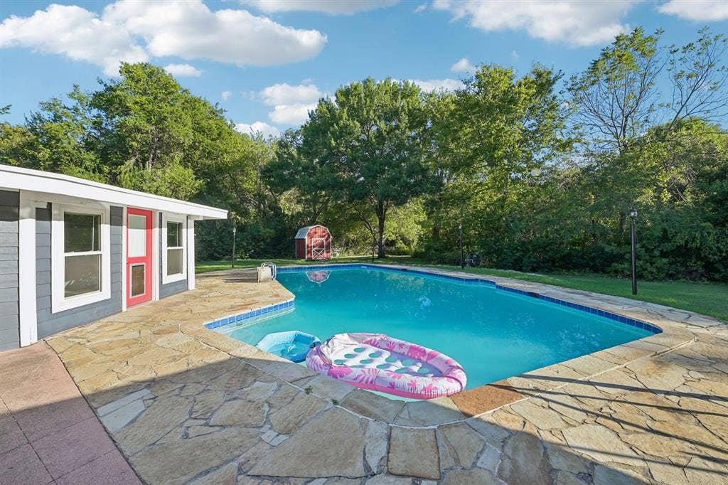 500 Spinner Road, DeSoto, TX 75115 Inviting swimming pool with natural stone decking and a pool house featuring a red entry door