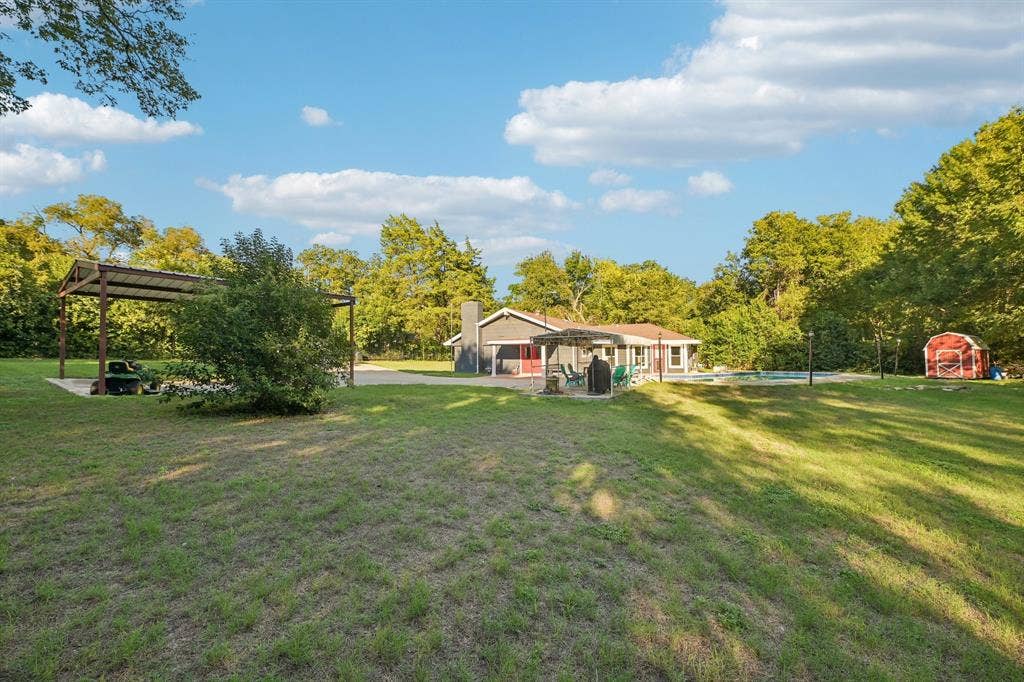 500 Spinner Road, DeSoto, TX 75115 Expansive lawn with a covered outdoor structure, mature trees, a red storage shed, and a visible pool
