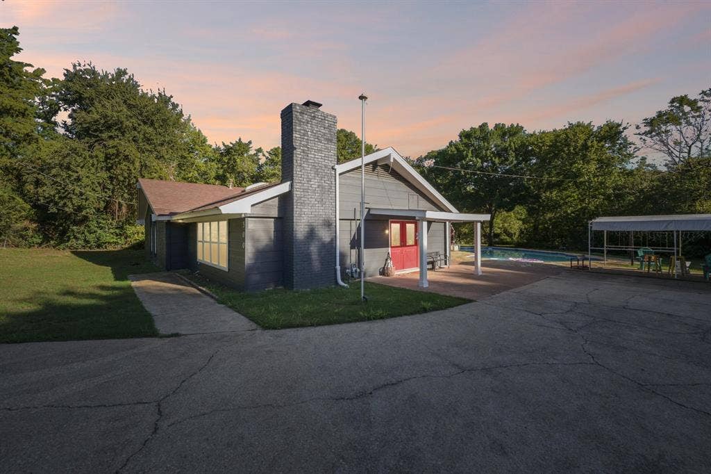 500 Spinner Road, DeSoto, TX 75115 Exterior featuring a grey siding finish, dark brick chimney, covered patio, and an in-ground pool