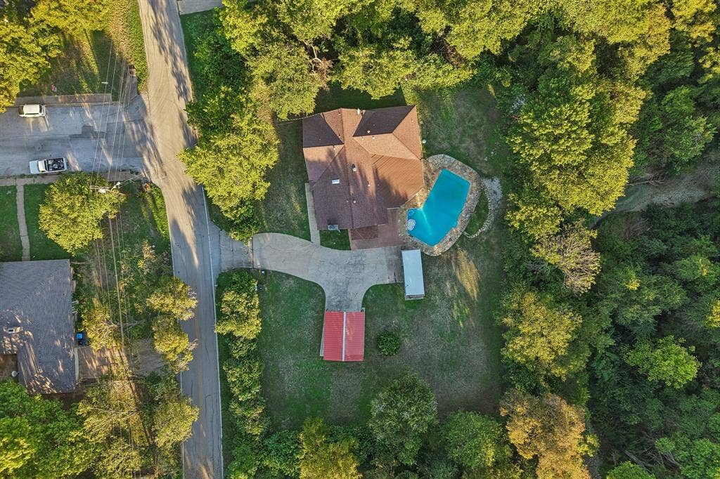 500 Spinner Road, DeSoto, TX 75115 Property featuring a multi-gabled roof, an irregular-shaped swimming pool with stone coping, a detached red-roofed structure, and a paved driveway