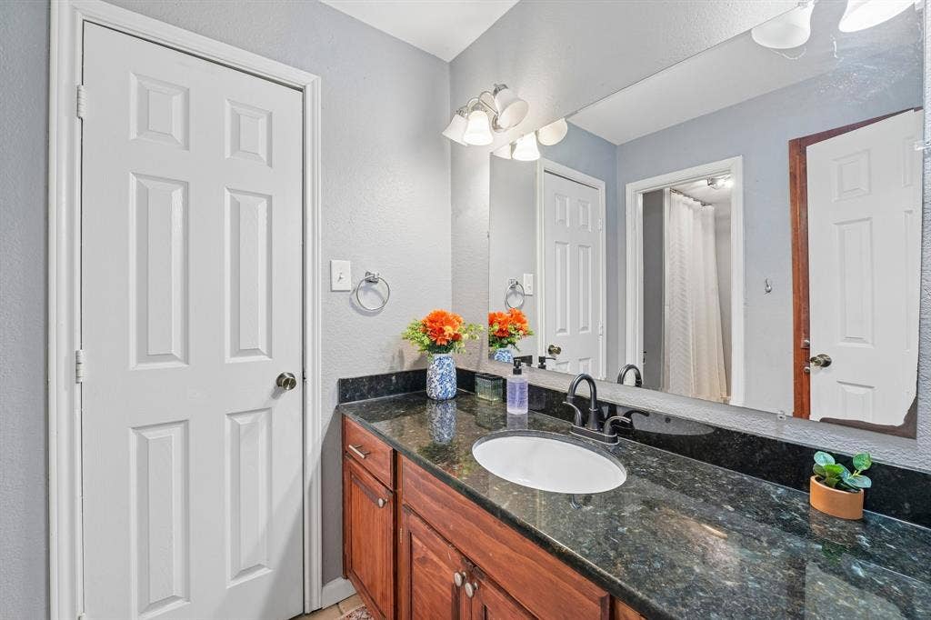 500 Spinner Road, DeSoto, TX 75115 Vanity with dark granite countertop, undermount sink, dark bronze faucet, and wood-finish cabinetry