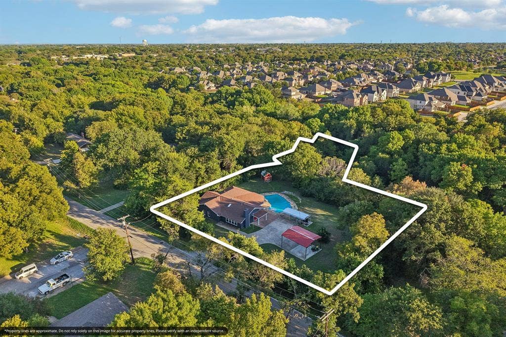 500 Spinner Road, DeSoto, TX 75115 Expansive property featuring a residence with a brown shingle roof, a blue-tiled swimming pool, a concrete driveway, and a red-roofed outbuilding, all surrounded by mature trees