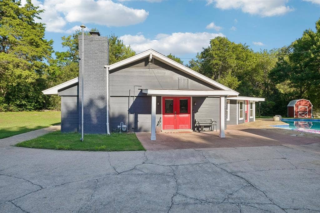 500 Spinner Road, DeSoto, TX 75115 Exterior featuring gray horizontal siding, a prominent brick chimney, red double entry doors, a covered patio, and an adjacent swimming pool