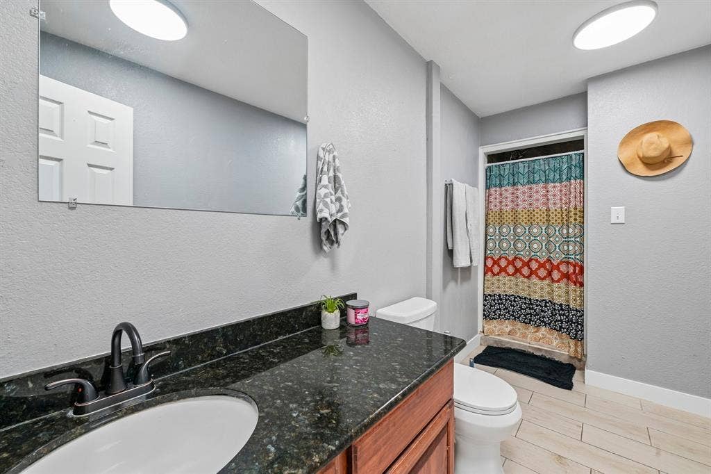 500 Spinner Road, DeSoto, TX 75115 Wood-finish vanity with an undermount sink, dark speckled countertop, and wall-mounted mirror