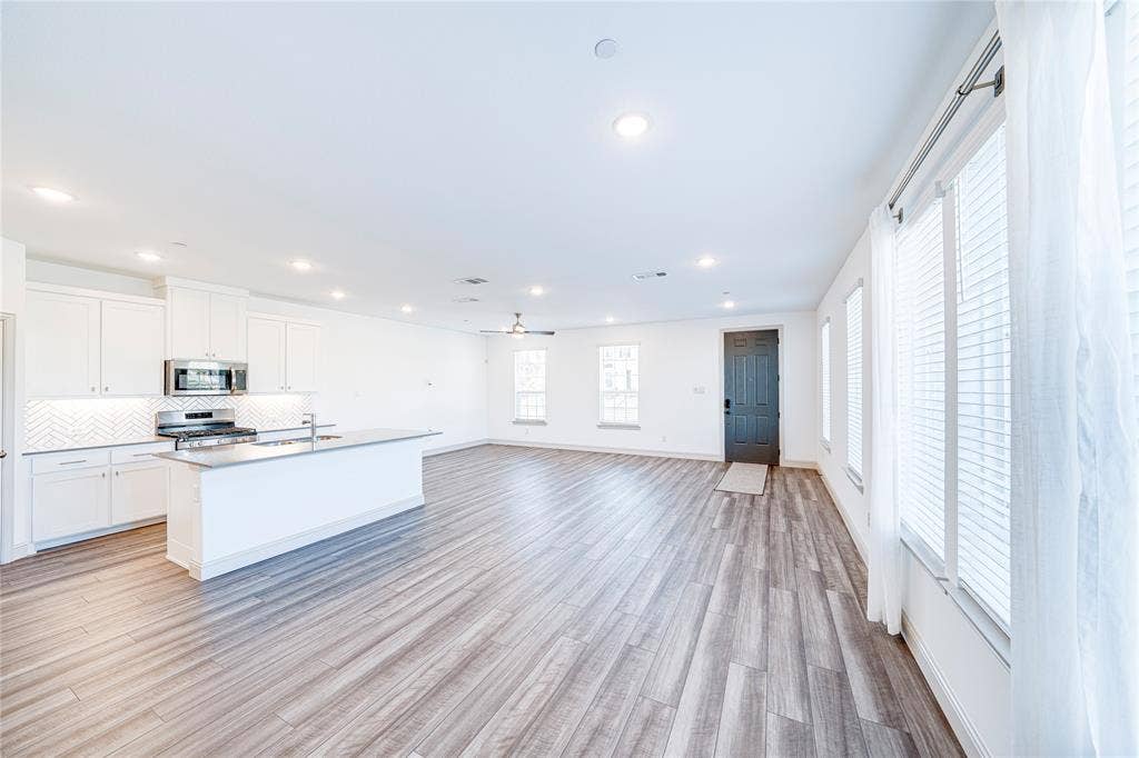 8888 Samara Street, Frisco, TX 75035 Open-concept living area featuring wood-finish flooring, recessed lighting, and multiple windows with blinds