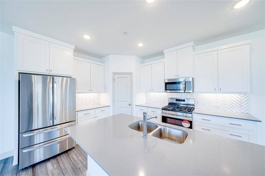 8888 Samara Street, Frisco, TX 75035 Kitchen featuring a large island with an undermount double-basin sink, stainless steel appliances, white cabinetry, herringbone tile backsplash, and recessed lighting