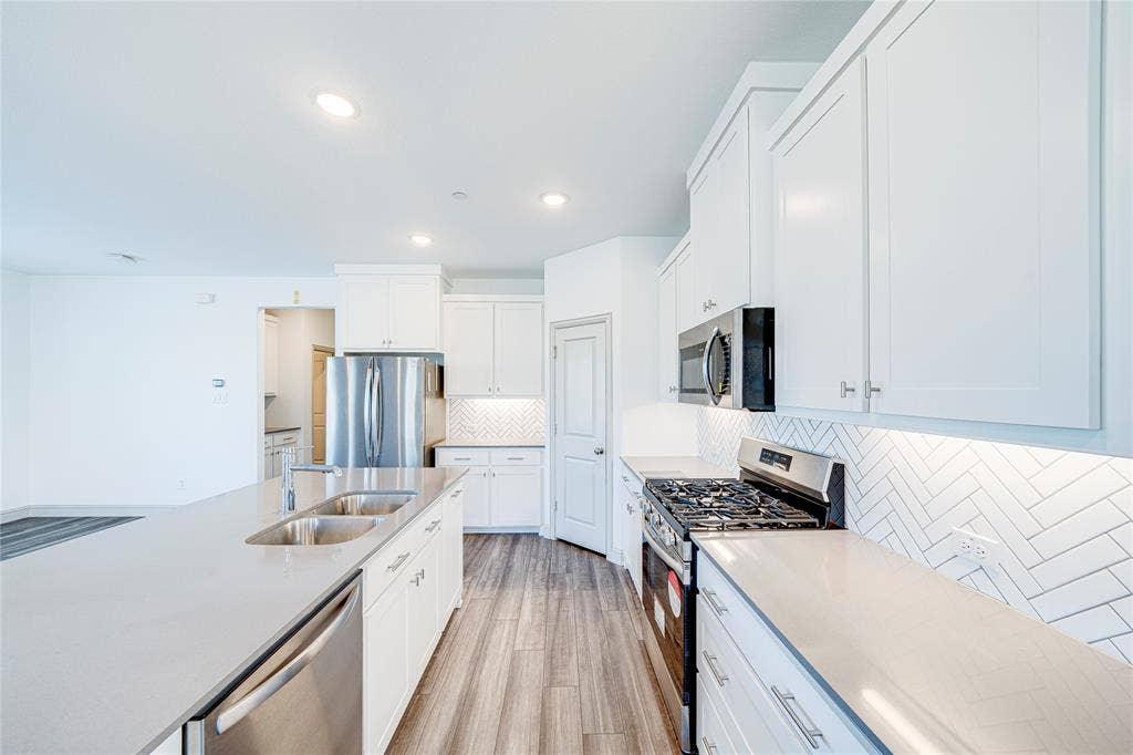 8888 Samara Street, Frisco, TX 75035 Modern kitchen featuring white cabinetry, stainless steel appliances, light countertops, a herringbone tile backsplash, and wood-finish flooring