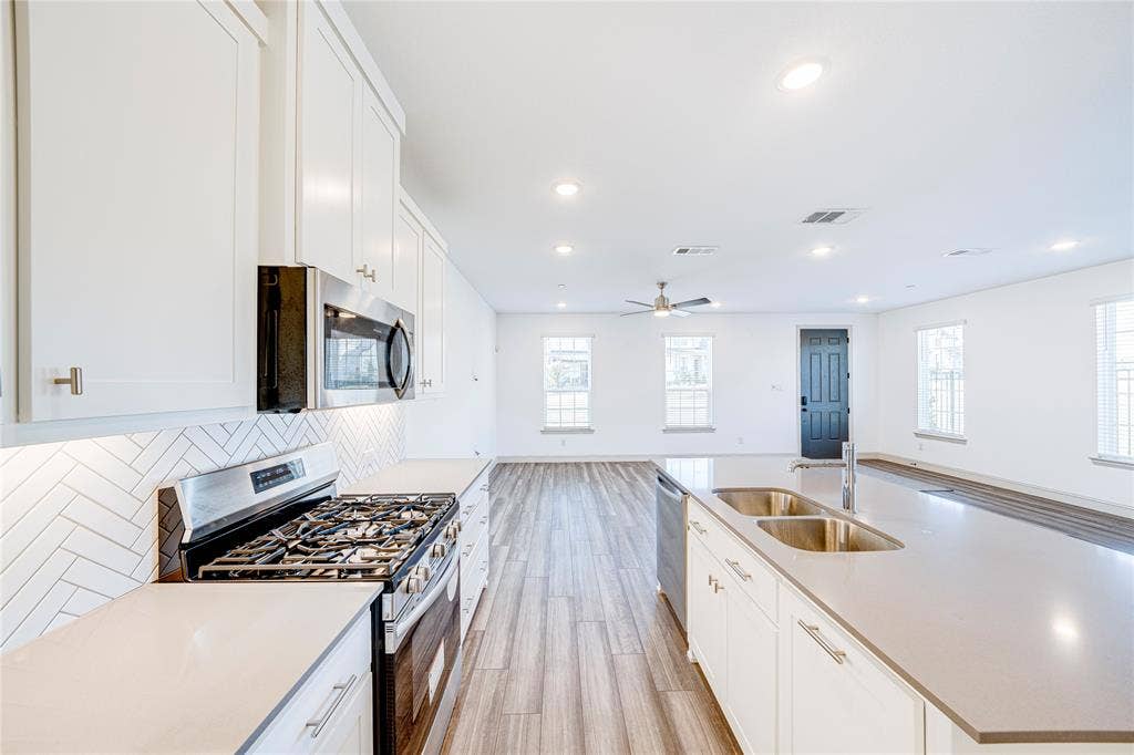 8888 Samara Street, Frisco, TX 75035 Sleek kitchen featuring white cabinetry, stainless steel appliances, a herringbone tile backsplash, and an expansive island with dual sinks